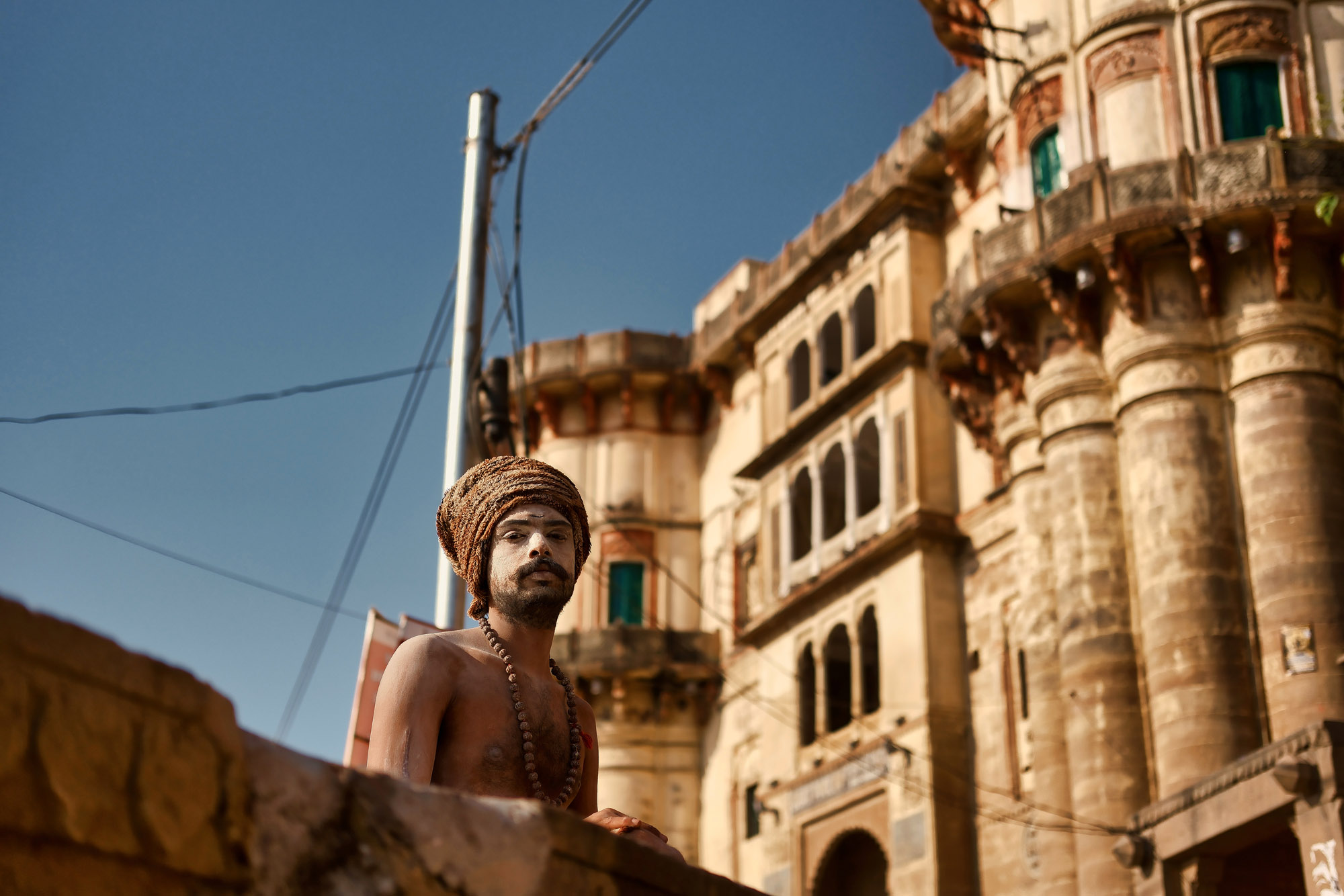 Sadhu con il volto coperto di cenere davanti ai palazzi dei ghat, Varanasi, Uttar Pradesh, India