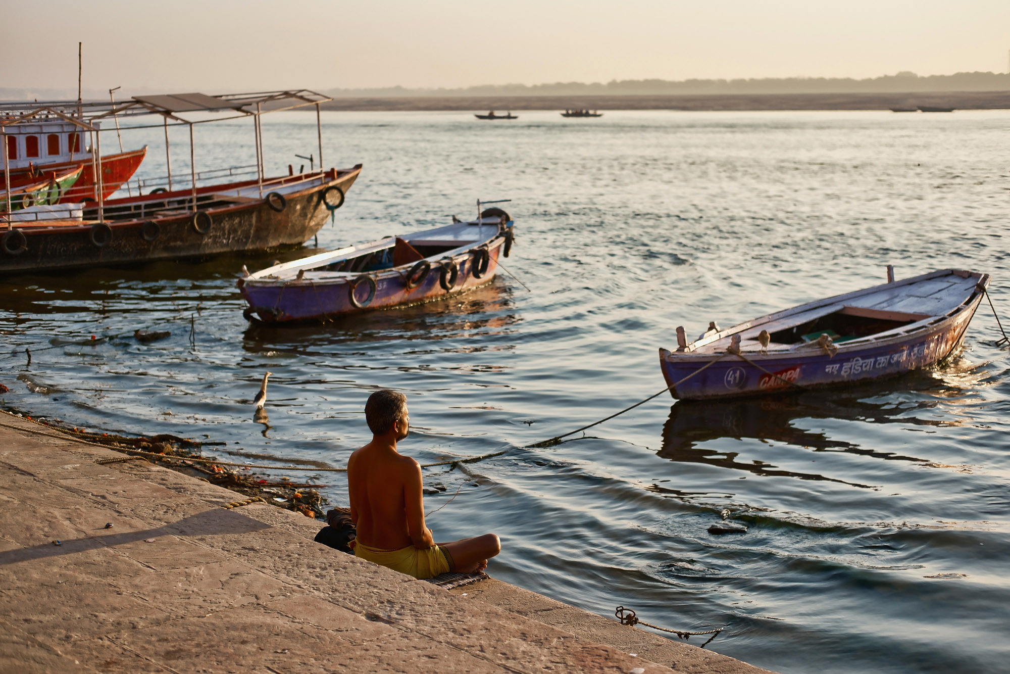 Uomo in meditazione davanti alle barche sul Gange